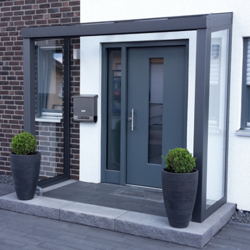 Moderne Eingangsüberdachung aus Aluminium mit Glaswänden und stilvollem Design.
